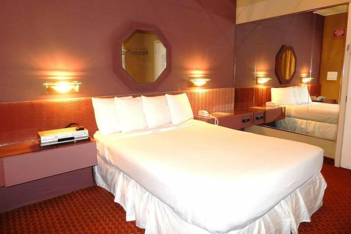 A hotel room with a large bed, bedside tables, a mirror, and wall-mounted lights.