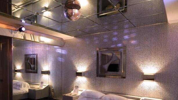 A modern hotel room with a large bed, a mirror, and wall-mounted lights. - Commack Inn (Commack)
