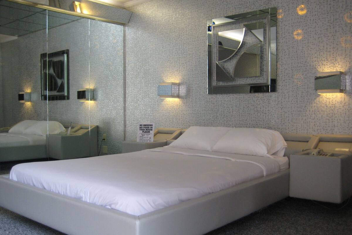 A modern hotel room with a large bed, bedside tables, a mirror, and a 'No Smoking' sign.