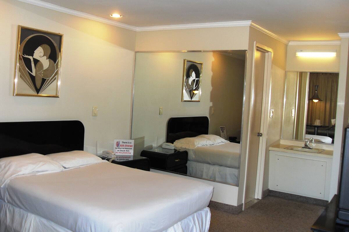 A hotel room with two beds, a desk, a mirror, and a bathroom visible through an open door.