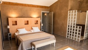 Une chambre moderne avec un grand lit, des tables de chevet, un banc et une cloison en verre.