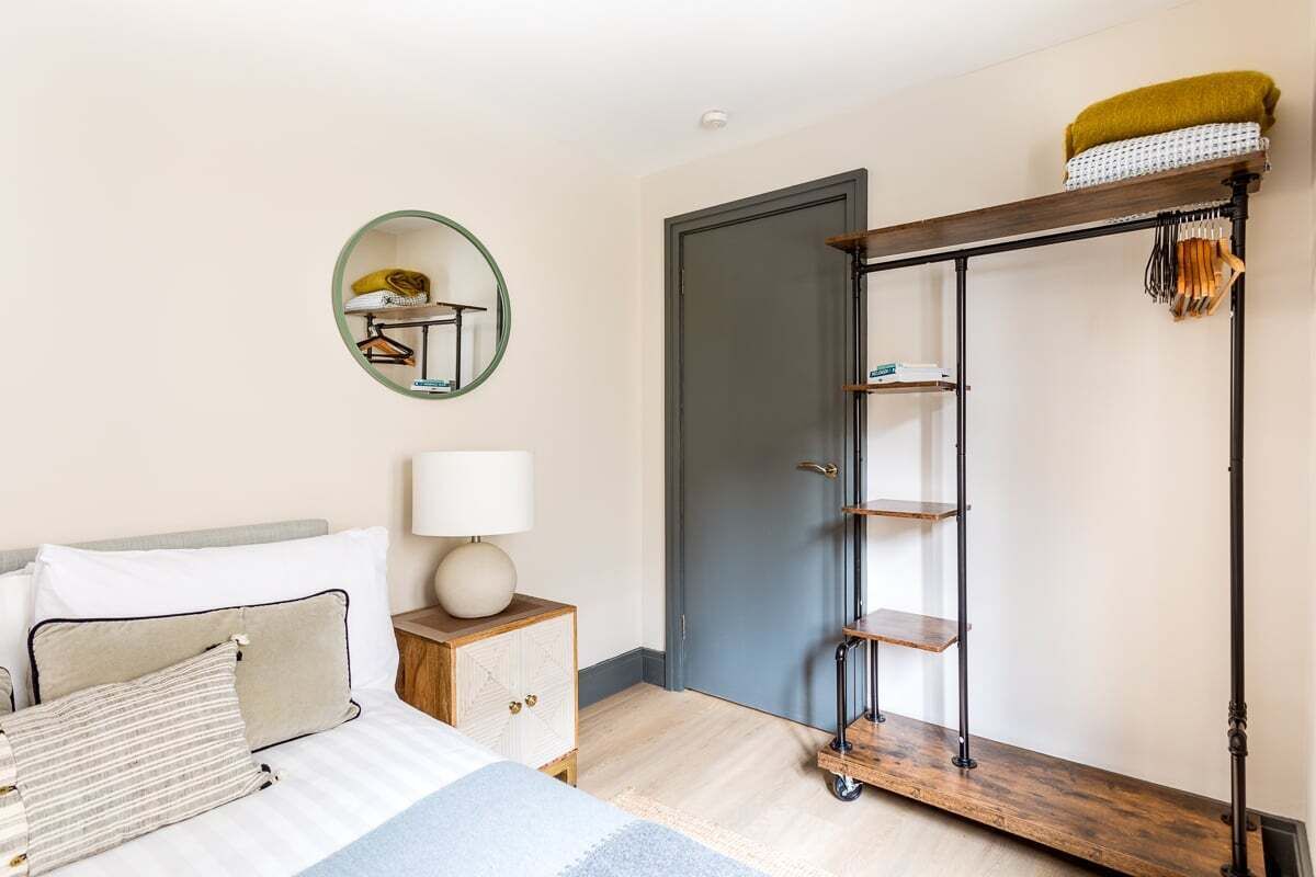 Une chambre à coucher comprenant un lit, une table de chevet, une lampe, une armoire et un miroir au mur.