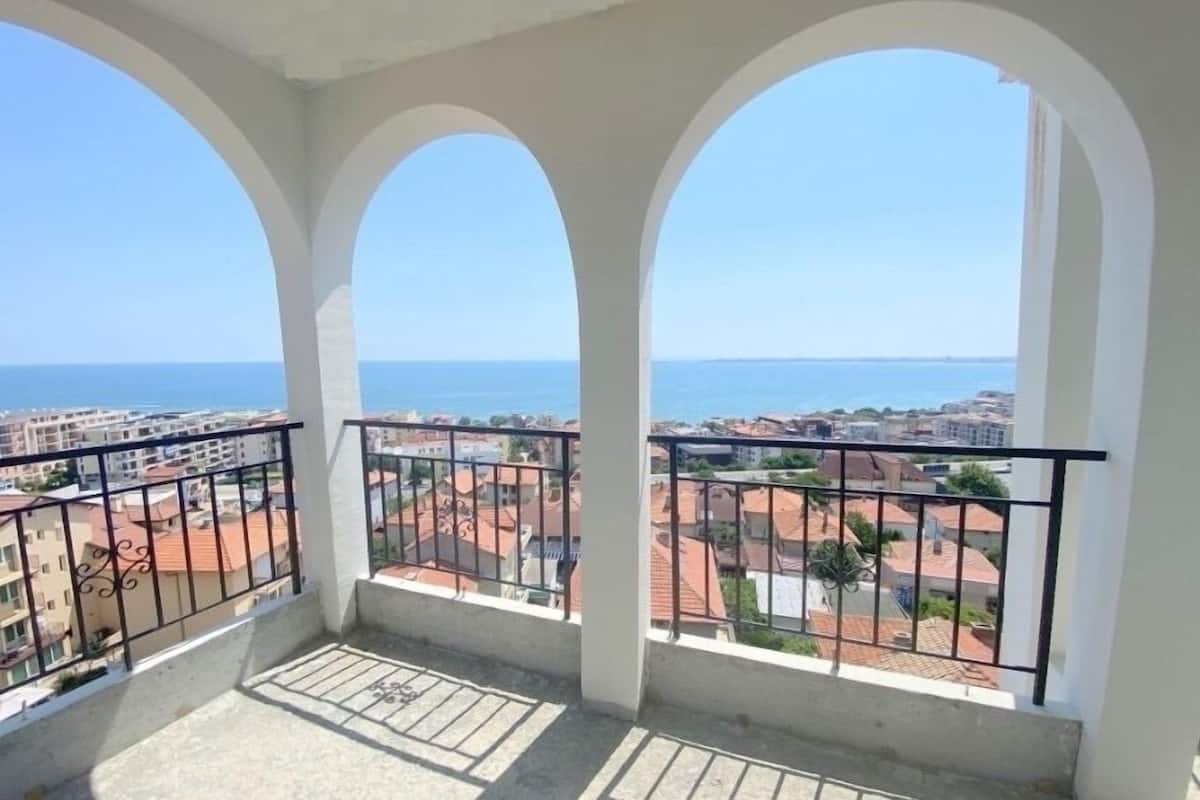 Un balcon doté de trois arcades, offrant une vue sur la mer et les bâtiments environnants.