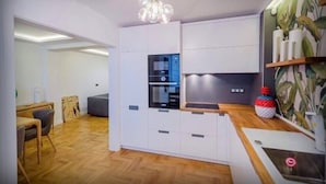 Moderni keittiö, jossa on valkoiset kaapit, sisäänrakennettu uuni ja puinen työtaso.
