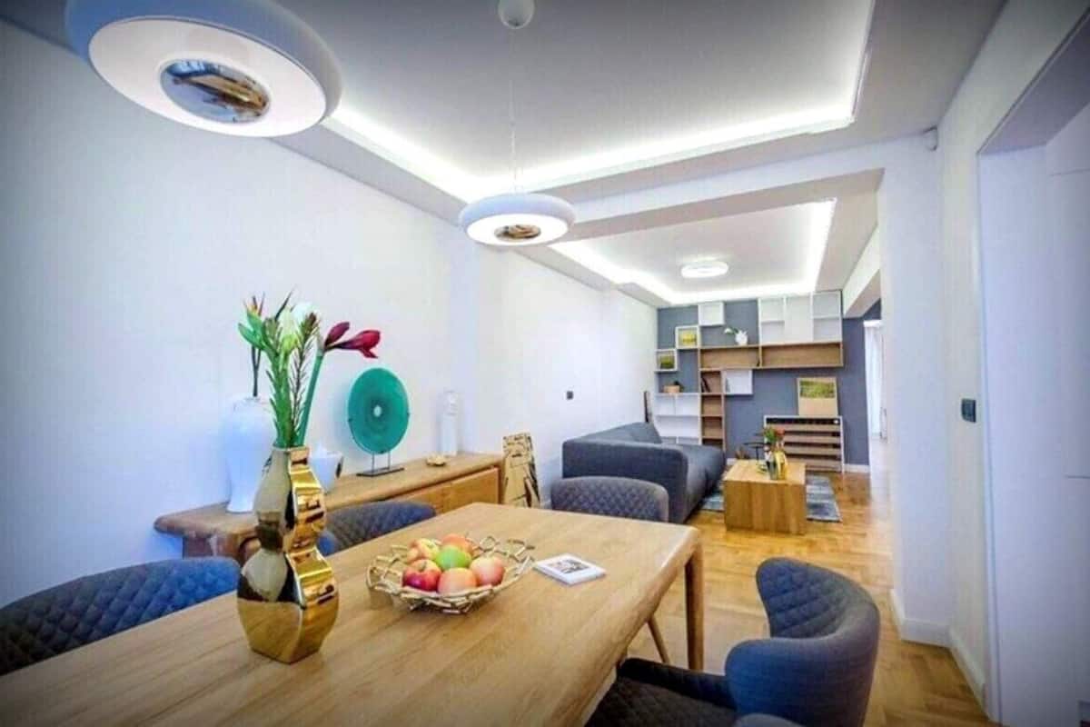Un salon moderne avec une table à manger en bois, des canapés bleus et un ventilateur vert.