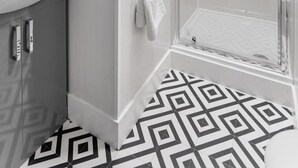 Ein modernes Badezimmer mit Duschabtrennung aus Glas, einem weißen Waschbecken und einem fußbodenbündigen, gemusterten Boden.