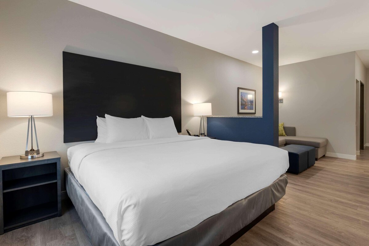 A modern hotel room with a large bed, bedside tables, a desk, and a seating area.