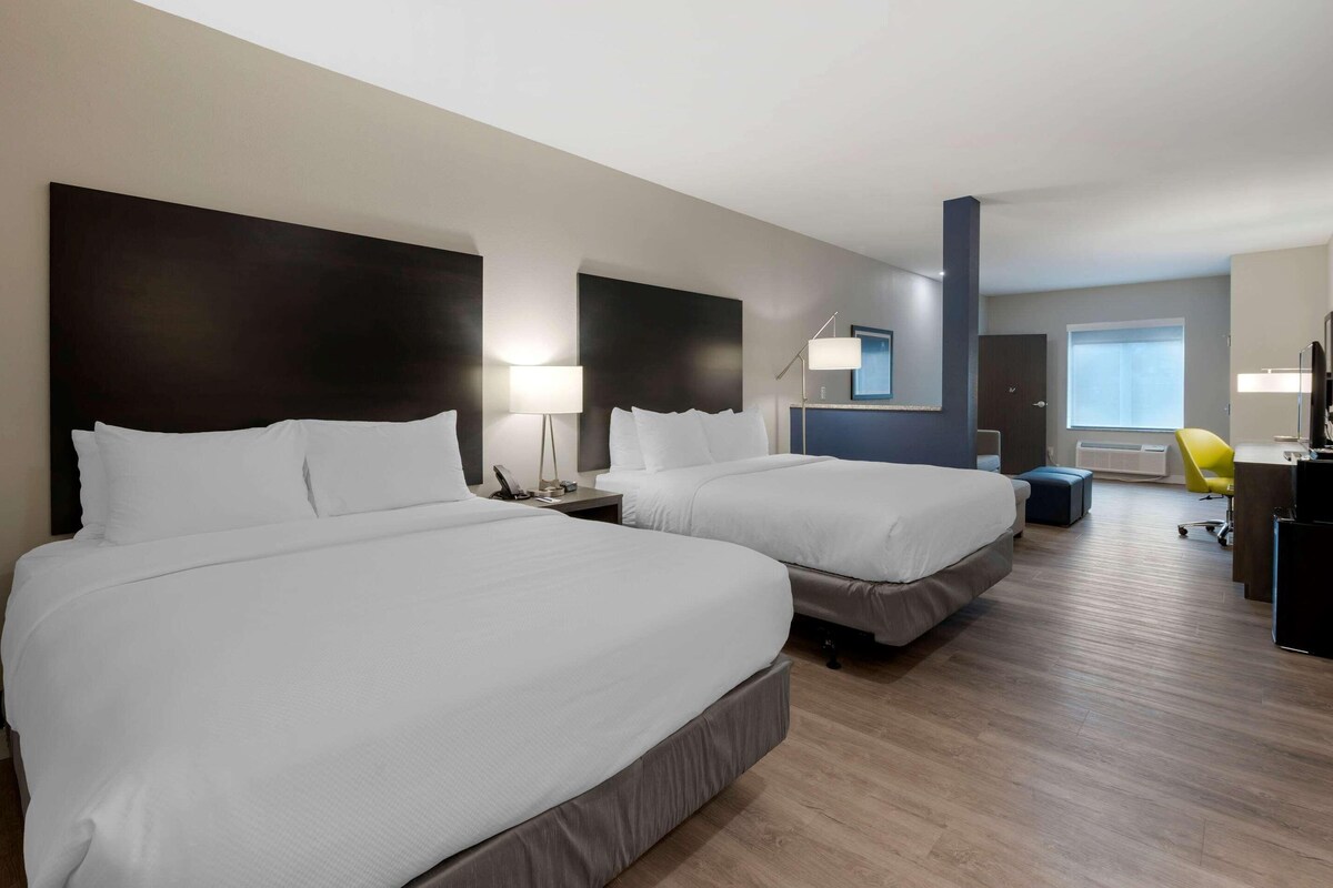 A hotel room with two beds, a desk, a chair, and a window.