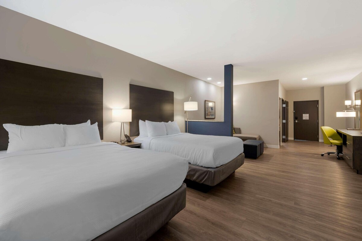 A hotel room with two beds, a desk, a chair, and a door.