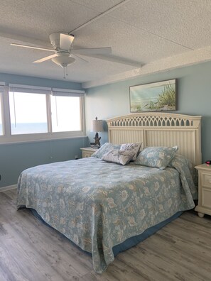 A bedroom with a bed, a ceiling fan, a nightstand, a lamp, and a painting on the wall.