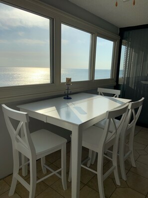 A dining area with a white table and chairs, large windows with a view of the sea, and a small decorative item on the table.