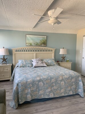 A bedroom with a bed, two nightstands, a ceiling fan, and a painting on the wall. - Direct Beachfront with pool (Ocean City)