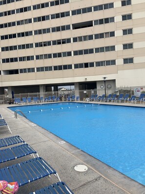 A swimming pool with blue water, surrounded by blue lounge chairs. - Direct Beachfront with pool (Ocean City)
