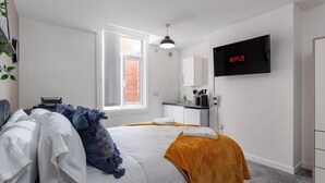 A modern bedroom with a bed, a TV mounted on the wall, a window, and a small kitchenette area. - Studio 5 • City Centre • Fast WiFi • Smart TV (Middlesbrough)