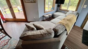 Ein gemütliches Zimmer mit einer großen Couch, einem Flachbildfernseher und einem Essbereich, der durch die Fenster sichtbar ist.