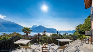 Une terrasse dotée de chaises longues et d’une table, offrant une vue sur un lac et des montagnes.