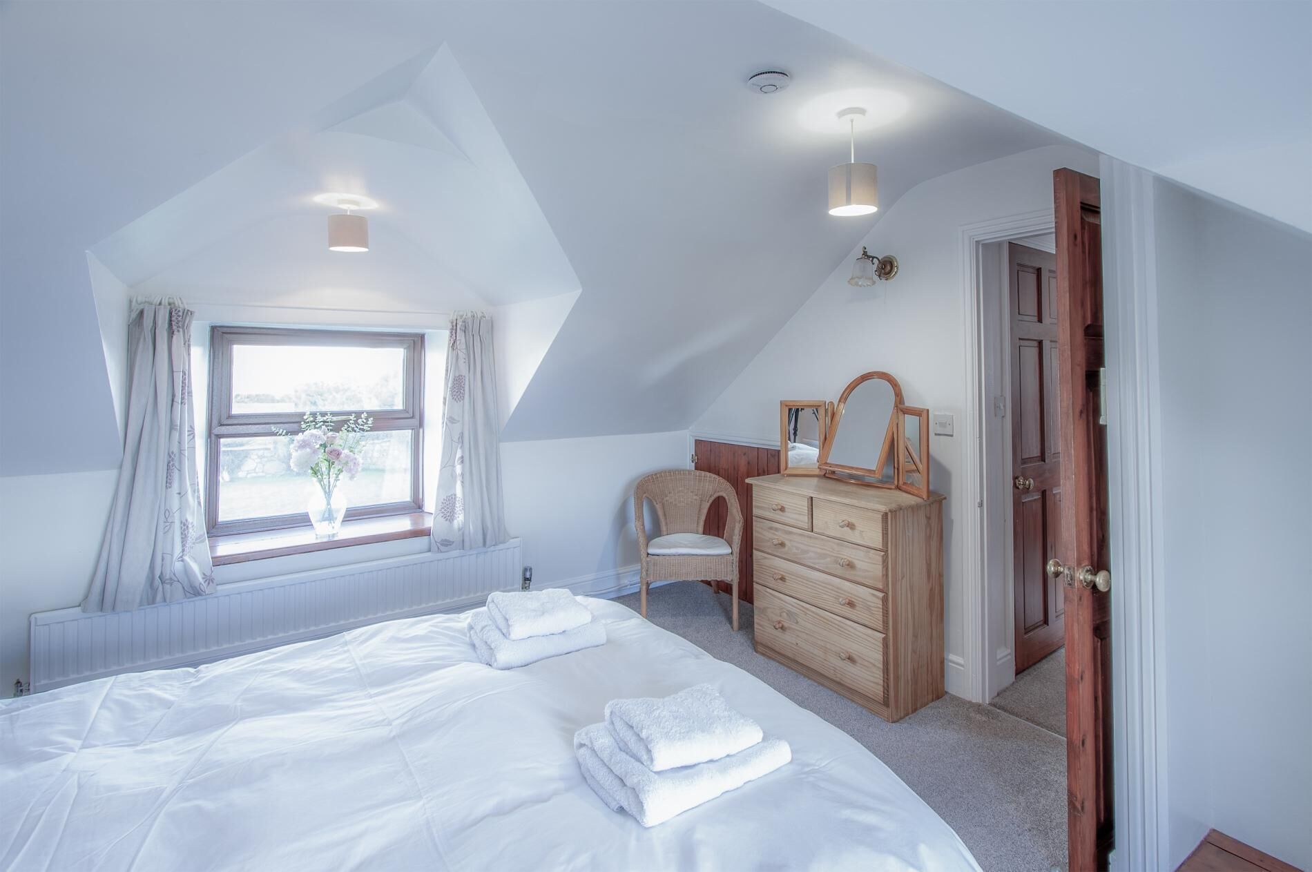 Une chambre avec un grand lit, une commode, une chaise et une fenêtre avec des rideaux.