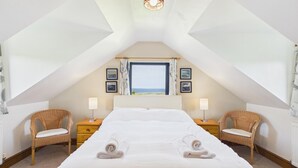 Una camera da letto con un letto grande, due poltrone in vimini, un comodino, una finestra vista e quadri appesi alle pareti.