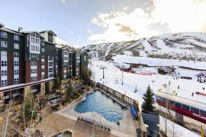 Un hotel con piscina, pistas de esquí y montañas al fondo.