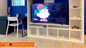 Ett vardagsrum med en platt-TV placerad på ett vitt TV-bord, en vit stol, en liten hylla med dekorativa föremål och en blå vägg.