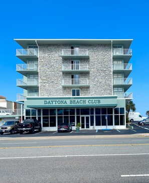 A building with the sign "Daytona Beach Club" on the front. It has multiple balconies and a stone facade.