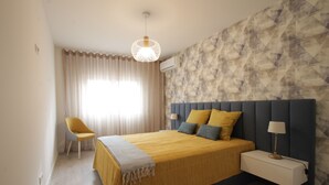 A bedroom with a bed, a chair, a bedside table, and a lamp.
