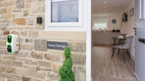 Un mur de pierres sur lequel est apposée une plaque indiquant « Eames Cottage », une petite haie verte et une fenêtre.