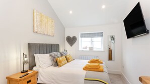 Une chambre à coucher comprenant un lit, une table de chevet, une lampe, des œuvres d’art murales et un téléviseur.