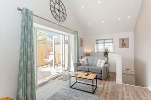Ein modernes Wohnzimmer mit grauem Sofa, einem Holztisch und einem großen Fenster mit Jalousien.