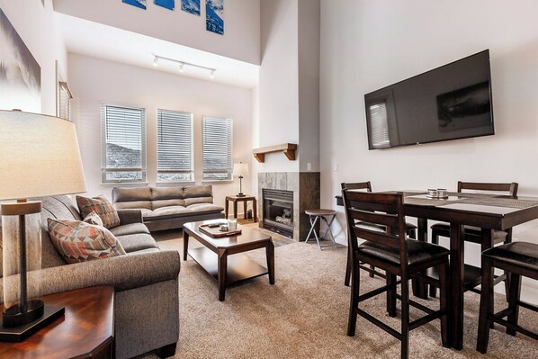 Ein geräumiges Wohnzimmer mit Kamin, einem Essbereich mit Tisch und Stühlen sowie einem großen Flachbildfernseher an der Wand.