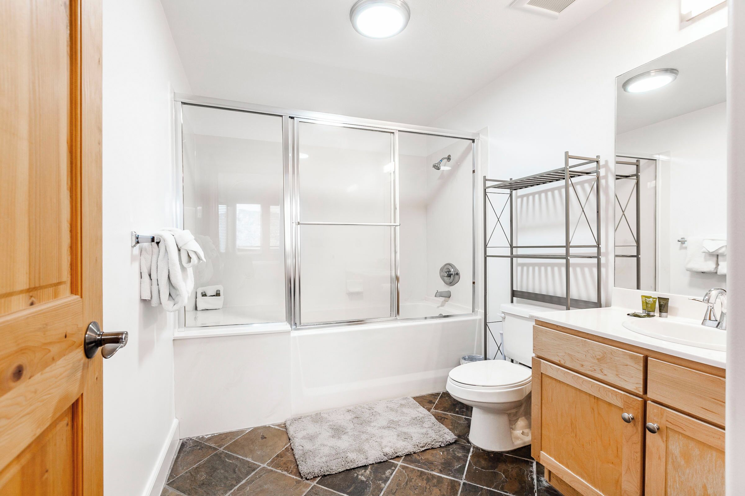 Une salle de bain moderne avec une douche à parois de verre, des toilettes blanches et un meuble-lavabo en bois avec un miroir.