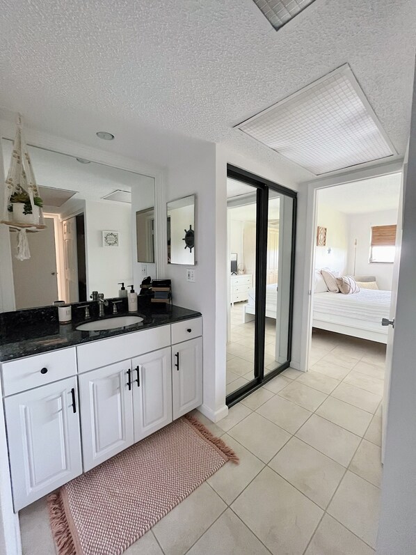 A modern bathroom with a large mirror, white cabinetry, a black countertop, and a beige rug.