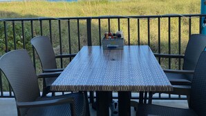 Un balcón con mesa y sillas, con vistas a un campo cubierto de hierba y el océano.