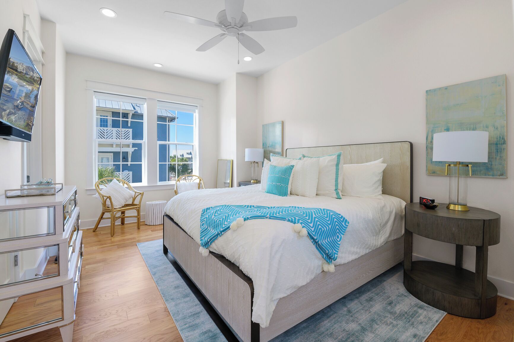A bedroom with a large bed, a ceiling fan, a TV, and a window with a view of buildings.