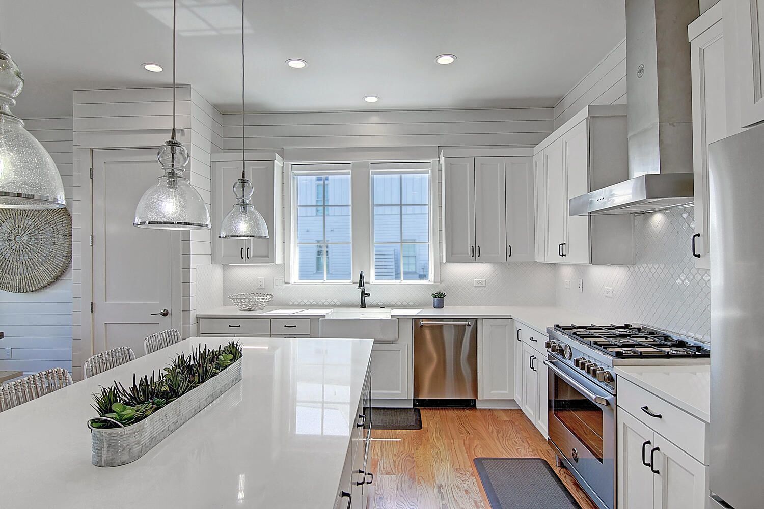 Una cocina moderna con armarios blancos, una isla central, electrodomésticos de acero inoxidable e iluminación colgante.