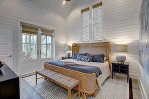 A bedroom with a large bed, a bench, two bedside tables, and a window with blinds. - Beachful Easy Feeling 117 CE (Port Aransas)