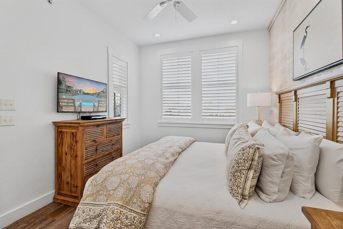A bedroom with a bed, a wooden dresser, a television, and a window with blinds.