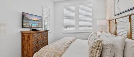 A bedroom with a bed, a wooden dresser, a television, and a window with blinds.
