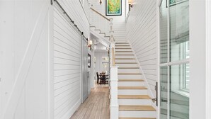 A staircase with white walls and wooden steps leading to a room with a dining table and chairs. - Blue Magnolia 217 LAK (Port Aransas)
