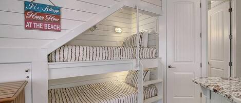 A bunk bed with three levels, a white door, and a small wooden bench.