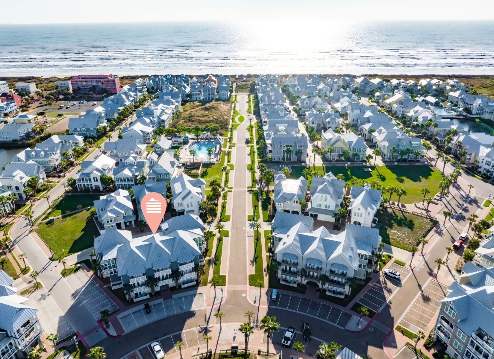 An aerial view of a coastal residential area with uniform white houses, a central road, and a beach in the background.