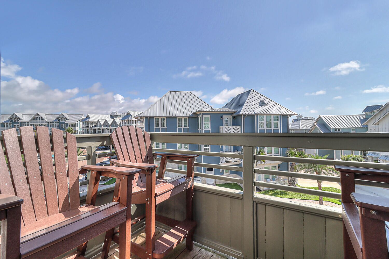 A balcony with wooden Adirondack chairs and a view of coastal houses.