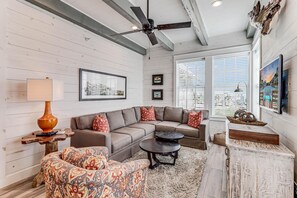 A modern living room with a sectional sofa, a patterned armchair, a coffee table, and a ceiling fan. - C View TC 1310 (Port Aransas)