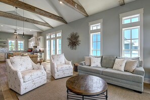 Un salon spacieux avec un canapé gris, deux fauteuils blancs et une table basse ronde.