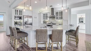 A modern kitchen with white cabinetry, stainless steel appliances, and a large island with bar stools. - Beyond Paradise 119 SE (Port Aransas)