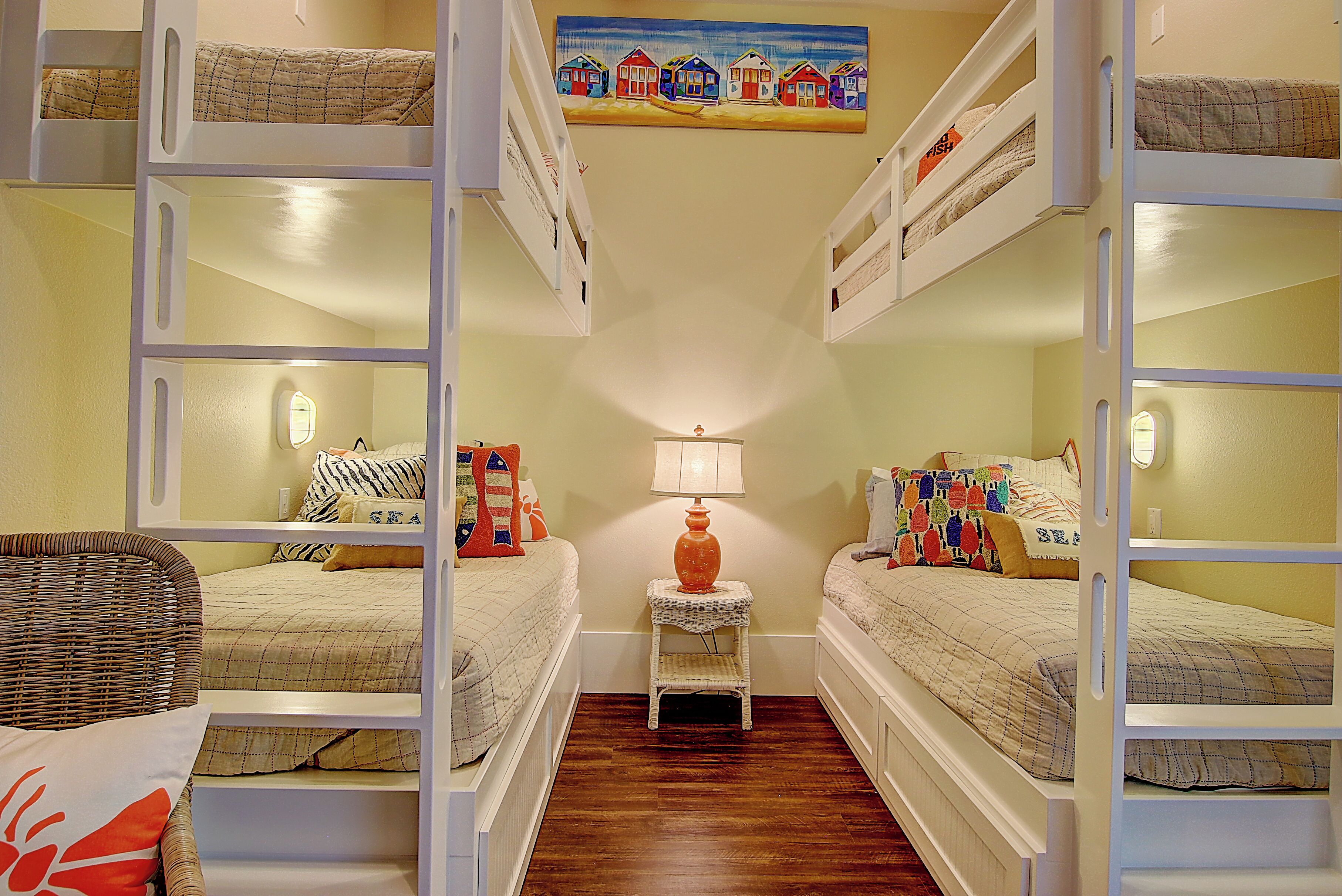 A room with bunk beds, a small table with a lamp, and a wicker chair.