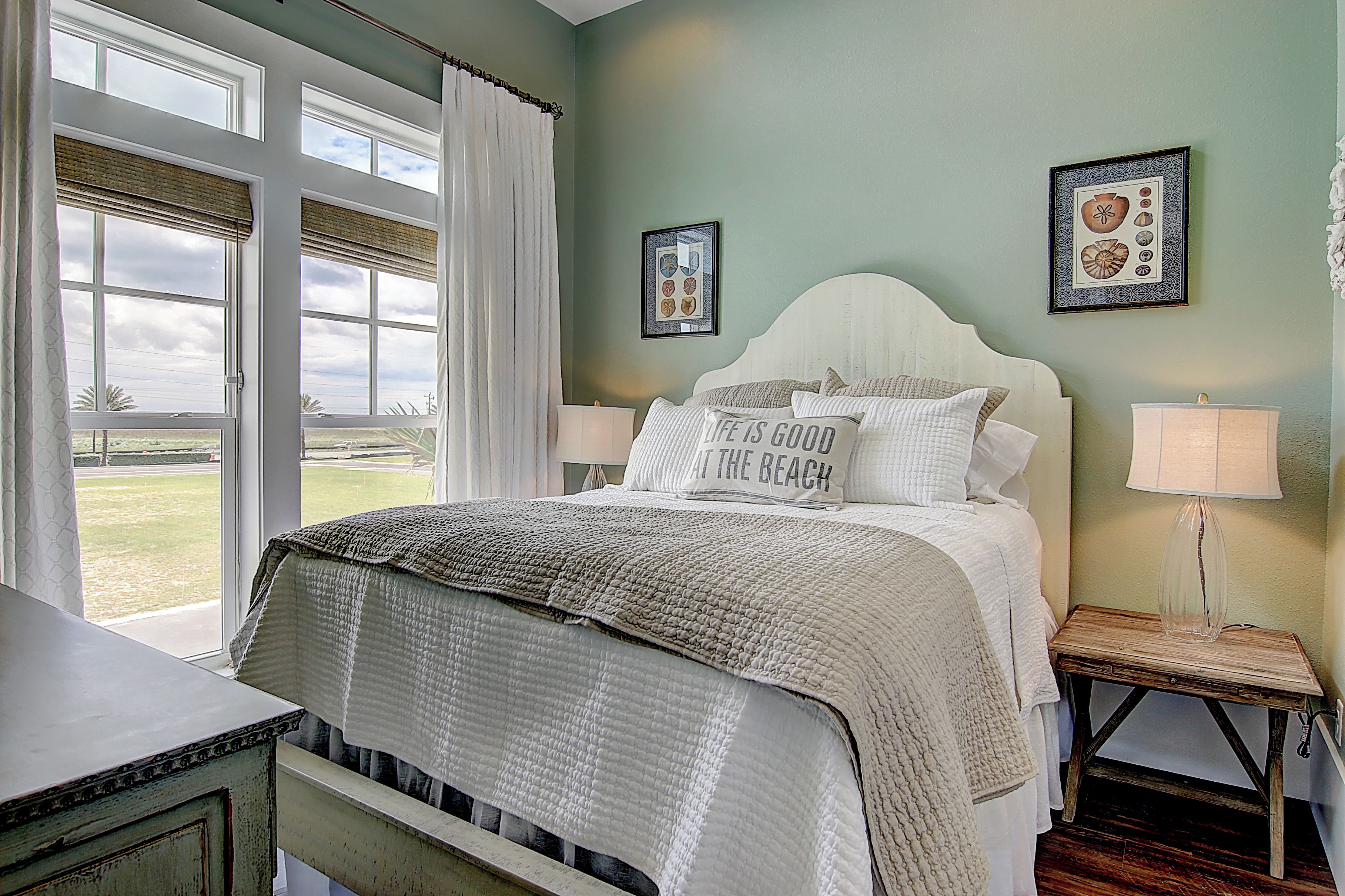 A bedroom with a large bed, a bedside table with a lamp, and a view of the outdoors through a window.