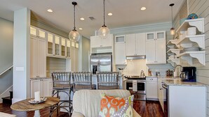 A spacious kitchen with white cabinetry, a dining area with wicker chairs, and a cozy seating area with a patterned throw pillow. - Beach Crush TC 7102 (Port Aransas)