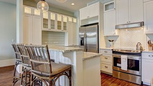 A kitchen with white cabinets, a stainless steel refrigerator, a built-in oven, and a hanging light fixture. - Beach Crush TC 7102 (Port Aransas)