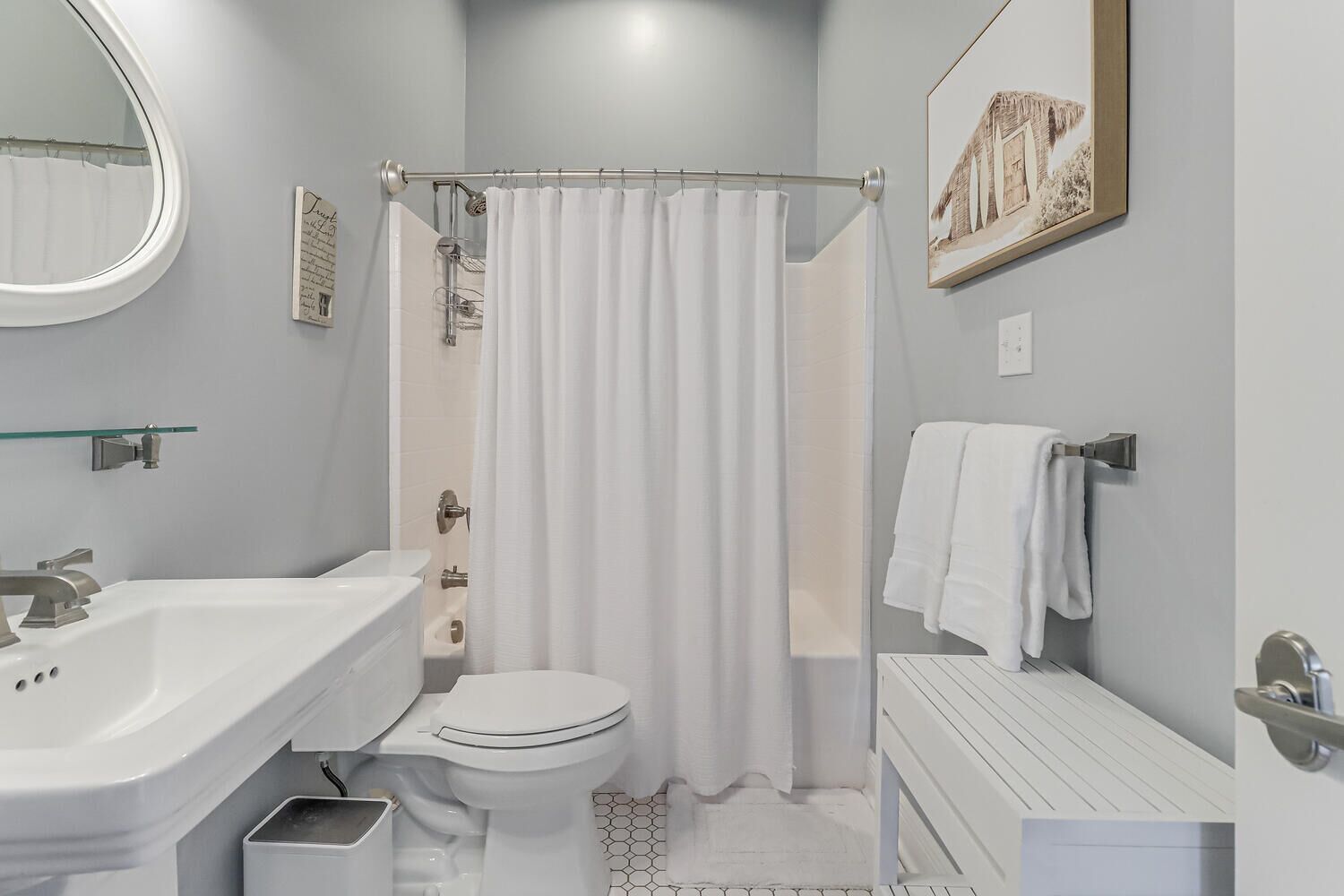 A modern bathroom with a white sink, toilet, and shower curtain. There is a framed picture on the wall and a towel rack with a towel.